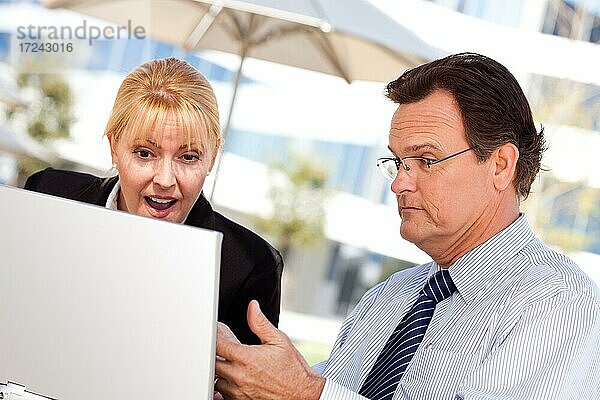 Gutaussehender Geschäftsmann arbeitet auf dem Laptop mit attraktiven weiblichen Kollegen im Freien