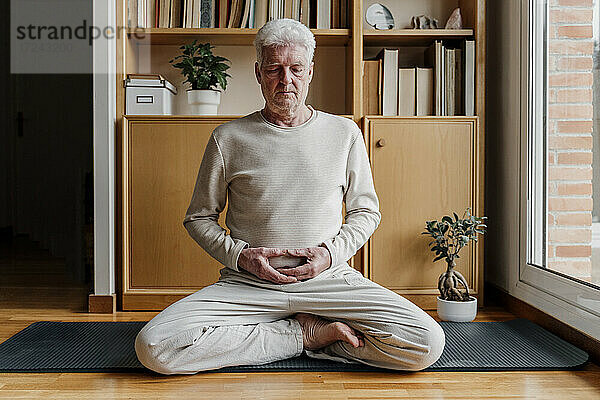 Älterer Mann beim Meditieren im Schneidersitz zu Hause