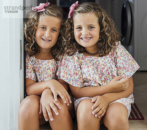 Lächelnde süße Schwestern sitzen zusammen an der Tür