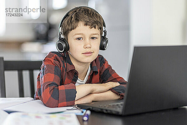 Junge mit Kopfhörern beim E-Learning  während er zu Hause am Laptop sitzt
