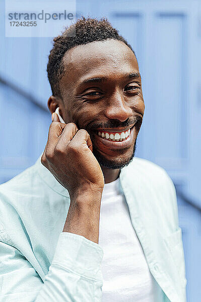 Lächelnder junger Mann in Freizeitkleidung mit In-Ear-Kopfhörern