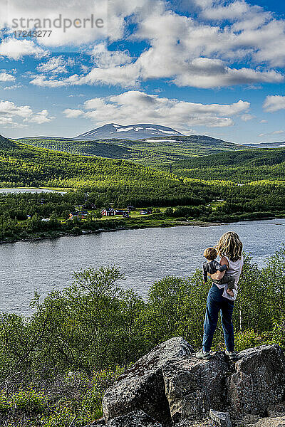 Mutter bewundert die Aussicht auf den Fluss Karasjohka mit ihrem kleinen Sohn in den Händen