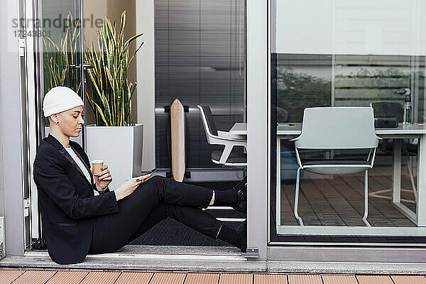 Junge Unternehmerin benutzt ein Mobiltelefon  während sie an der Tür sitzt
