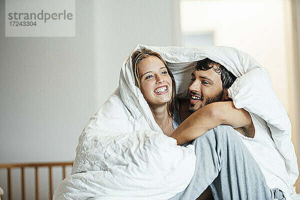 Glückliches Paar sitzt zu Hause unter einer Decke