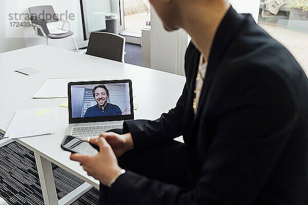 Geschäftsfrau  die einen männlichen Kollegen bei einem Videoanruf über einen Laptop im Büro beobachtet