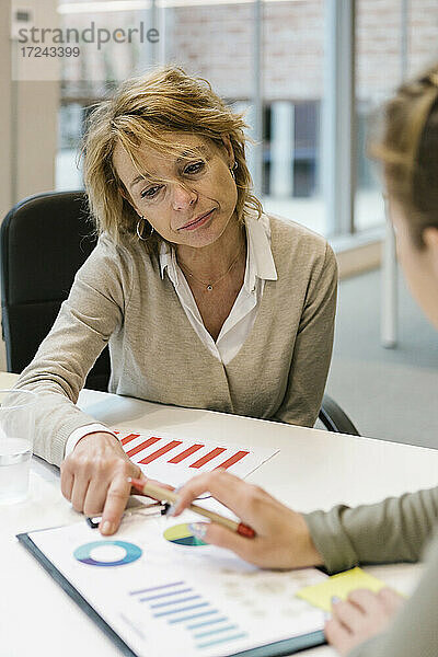 Reife Geschäftsfrau  die einer Mitarbeiterin am Schreibtisch in einem Coworking-Büro eine Grafik erklärt