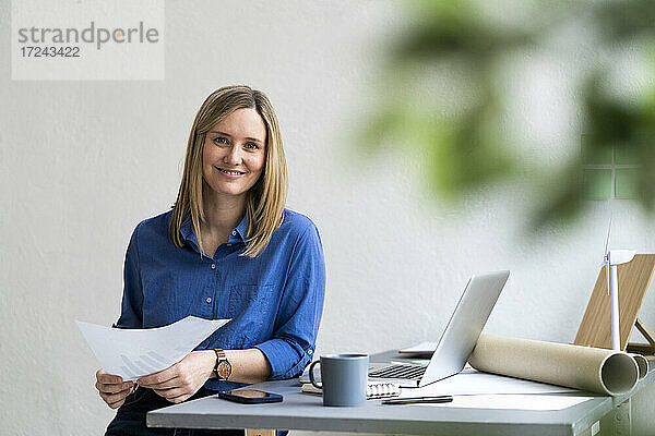 Lächelnde Geschäftsfrau sitzt mit Papier im Büro