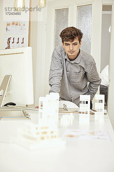 Männlicher Architekt  der ein Architekturmodell betrachtet  während er sich auf einen Tisch stützt
