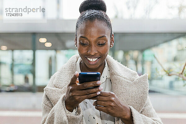Lächelnde Frau im mittleren Erwachsenenalter  die eine Textnachricht über ihr Smartphone sendet