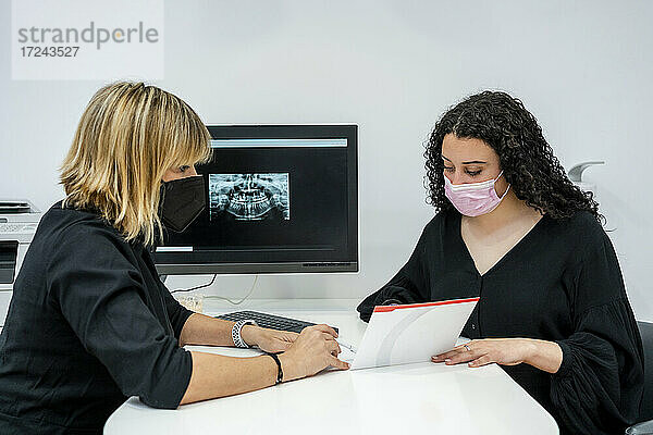 Eine Zahnärztin erklärt einem Patienten am Schreibtisch einen medizinischen Bericht während einer Pandemie