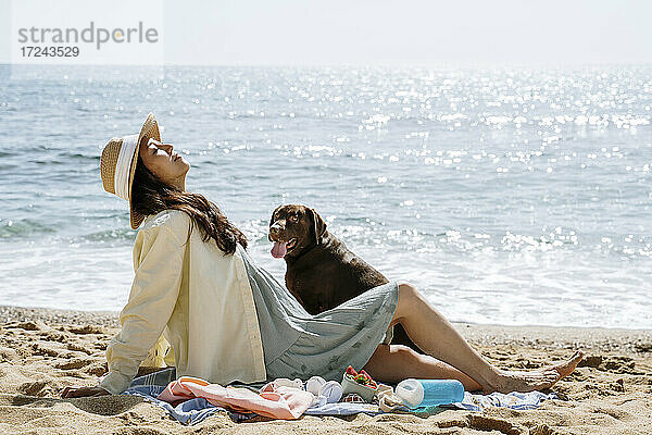 Mittlere erwachsene Frau entspannt sich mit Hund am Strand an einem sonnigen Tag