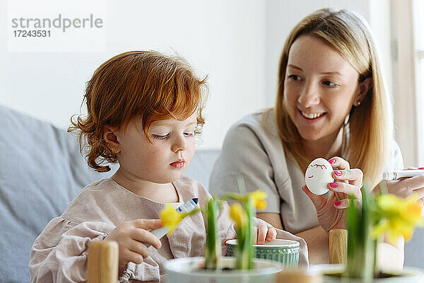 Lächelnde Mutter zeigt ihrer Tochter zu Hause ein Osterei