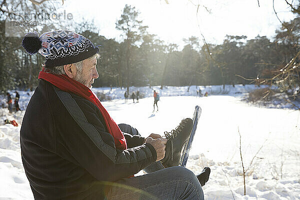 Älterer Mann trägt Schlittschuhe  während er im Winter auf Schnee sitzt