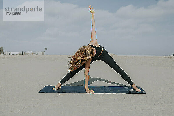 Weibliche Athletin übt Yoga auf einer Übungsmatte am Strand