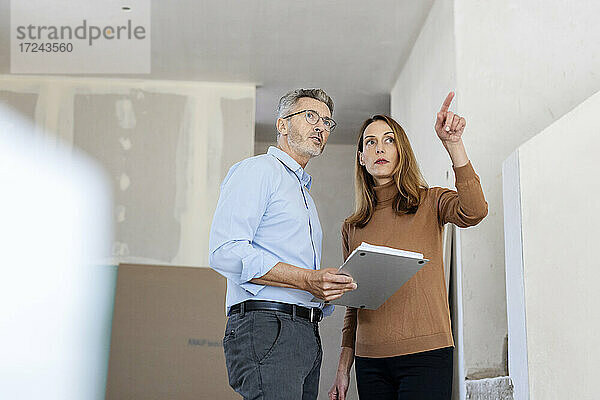 Ein weiblicher Kollege zeigt auf einen männlichen Architekten auf einer Baustelle und steht daneben