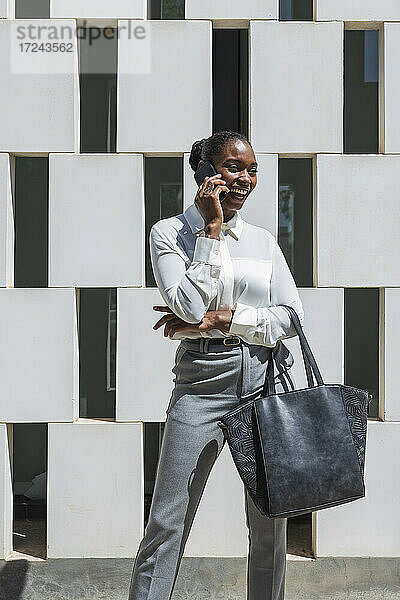 Fröhliche Geschäftsfrau  die vor einer Wand mit einem Mobiltelefon spricht