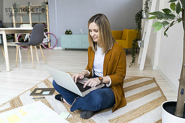 Weibliche kreative Geschäftsfrau mit Laptop auf Teppich im Büro