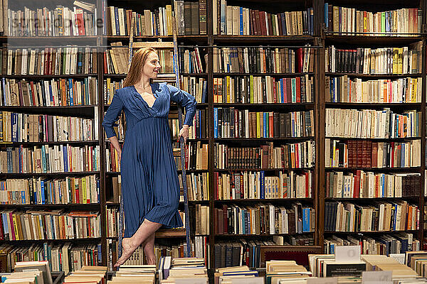Lächelnde Frau schaut weg  während sie auf einer Leiter in einer Bibliothek steht