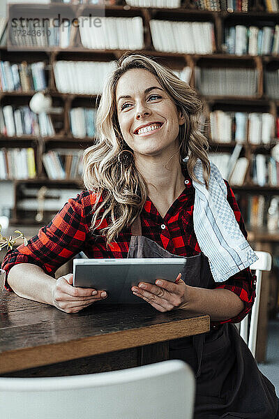 Lächelnde Besitzerin mit digitalem Tablet  die im Café wegschaut