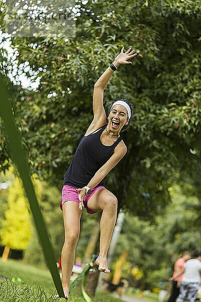 Fröhliche junge Sportlerin beim Slacklinen im Park