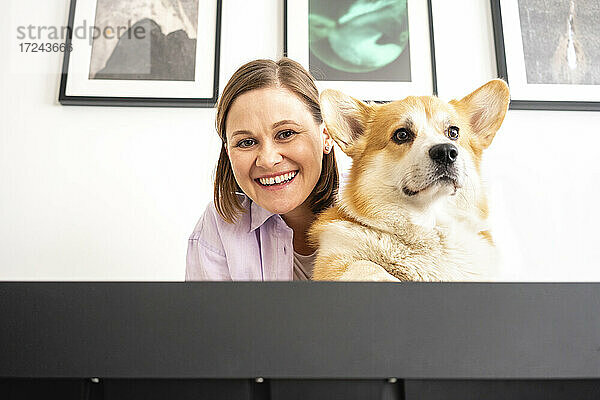Schöne lächelnde Frau mit Hund vor der Wand zu Hause
