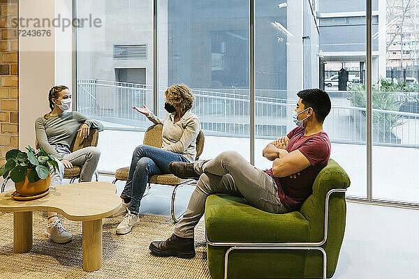 Weibliche Fachkräfte diskutieren mit jungen Kollegen in der Büro-Lobby während der COVID-19