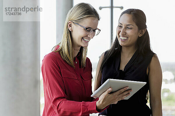 Lächelnde Geschäftsfrau  die ein digitales Tablet von einer Kollegin im Büro benutzt