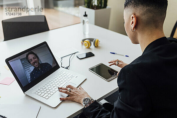Eine Unternehmerin benutzt ein digitales Tablet während eines Videogesprächs über einen Laptop im Büro