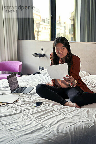 Geschäftsfrau liest ein Dokument  während sie auf dem Bett im Hotel sitzt
