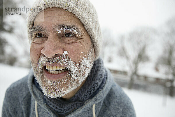 Lächelnder Mann  der im Winter mit Schnee im Gesicht wegschaut