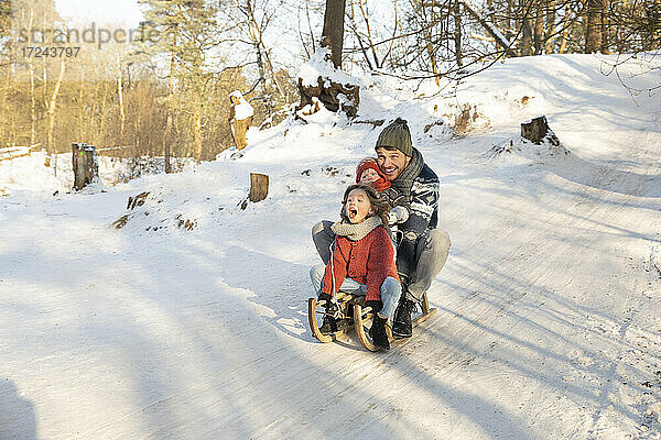 Verspielter Junge schlittert mit Vater und Bruder im Winter durch den Schnee