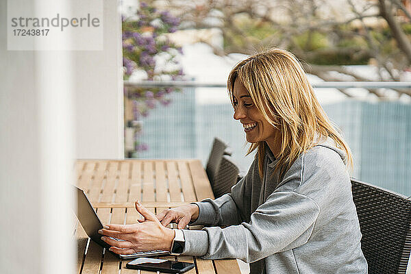 Lächelnde Berufstätige mit Laptop auf dem Balkon zu Hause