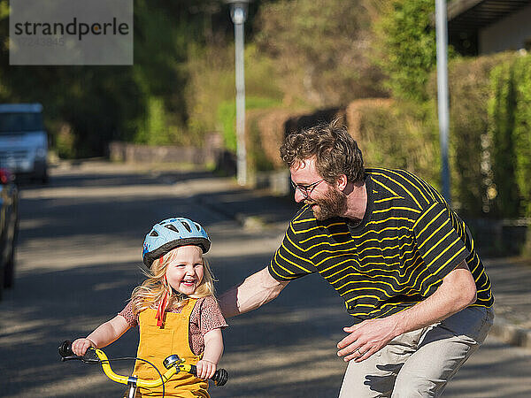 Glücklicher Vater bringt seiner Tochter im Freien das Radfahren bei