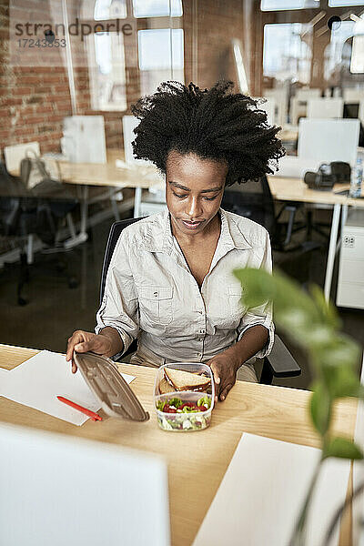 Afro-Geschäftsfrau beim Öffnen eines Containers in der Mittagspause im Büro