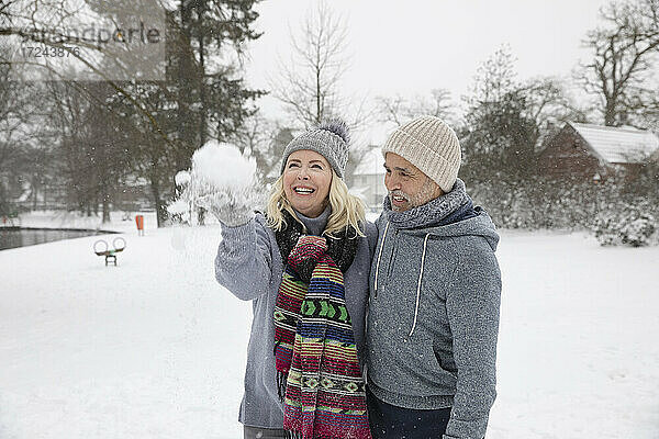 Fröhliche Frau wirft Schnee  während sie mit einem Mann im Park steht