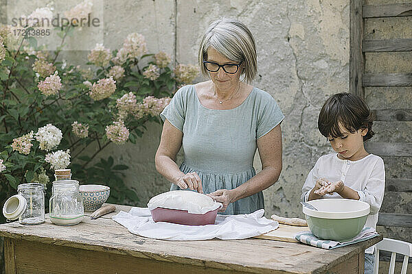 Großmutter bereitet Brot vor  während der Enkel im Garten mit Teig spielt