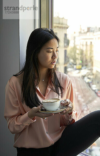 Geschäftsfrau hält Kaffeetasse und blickt durch das Fenster eines Hotels