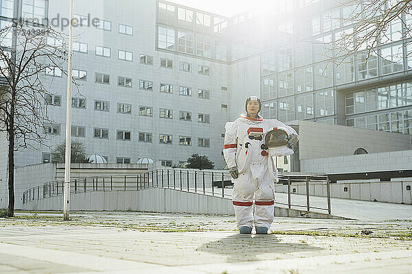 Weibliche Astronautin mit Weltraumhelm vor einem Gebäude in der Stadt an einem sonnigen Tag