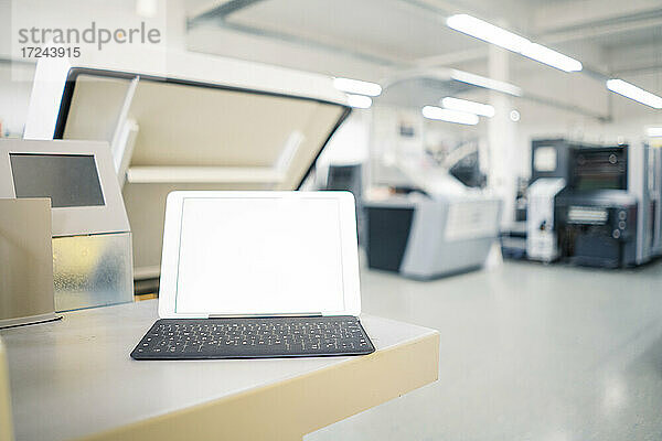 Digitales Tablet auf dem Tisch mit Druckmaschine in der Fabrik