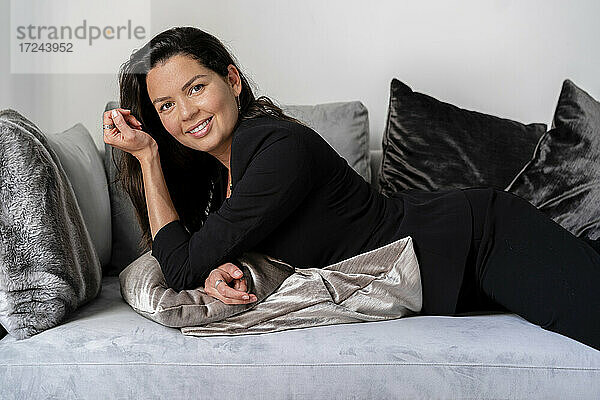 Lächelnde Frau  die sich zu Hause auf dem Sofa mit einem Kissen ausruht