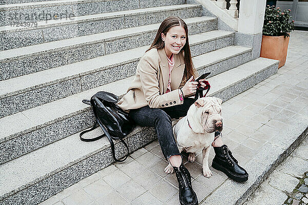 Lächelnde Frau mit Hund und Mobiltelefon auf einer Treppe sitzend