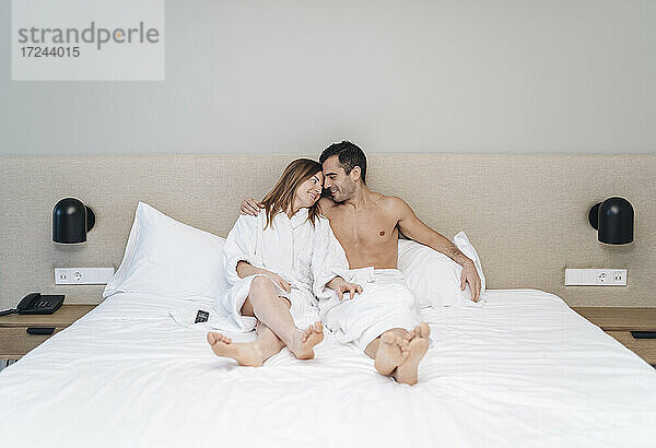 Mann mit Arm um eine umarmende Frau  die auf einem Bett in einem Hotelzimmer sitzt