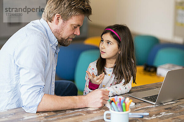 Mädchen gestikuliert beim Gespräch mit dem Vater während des E-Learnings am Tisch