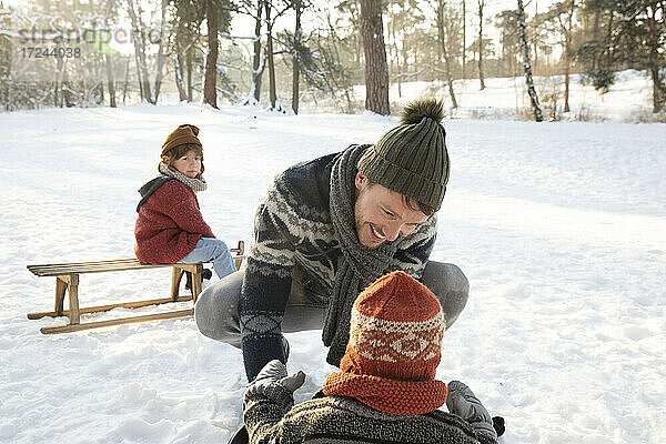 Lächelnder Vater in warmer Kleidung  der im Winter mit seinem Sohn im Schnee spielt