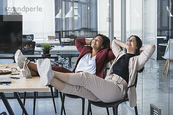 Lächelnde weibliche Fachkräfte mit geschlossenen Augen entspannen sich auf einem Stuhl in einem Coworking-Büro