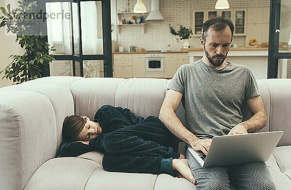 Der Sohn schläft neben dem Vater auf dem Sofa und benutzt einen Laptop