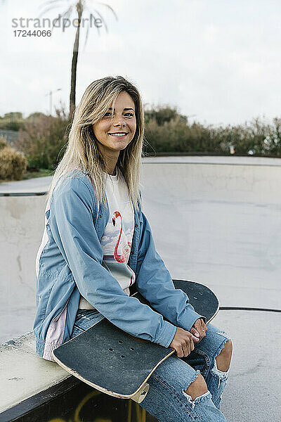 Lächelnde Frau  die ein Skateboard hält  während sie im Park sitzt