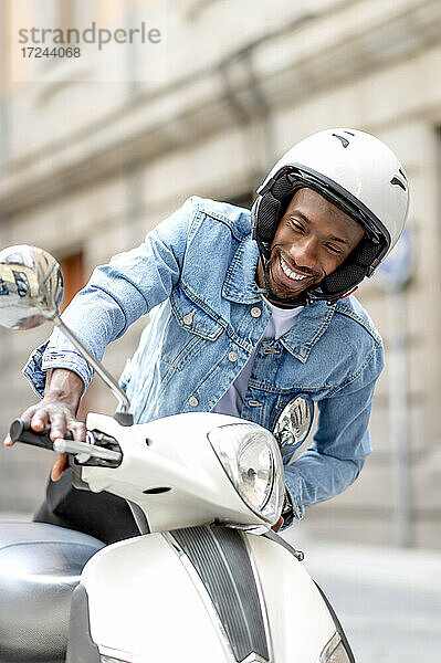 Junger Mann mit Sturzhelm beim Aufsteigen auf einen Motorroller