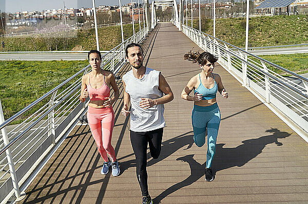Männliche und weibliche Athleten schauen beim Laufen auf einer Brücke an einem sonnigen Tag weg