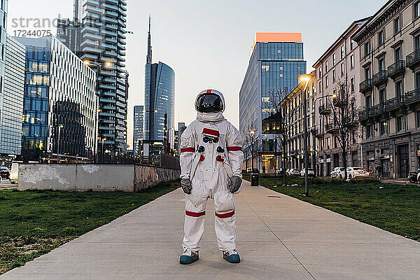 Männlicher Astronaut steht auf einem Fußweg inmitten von Gebäuden